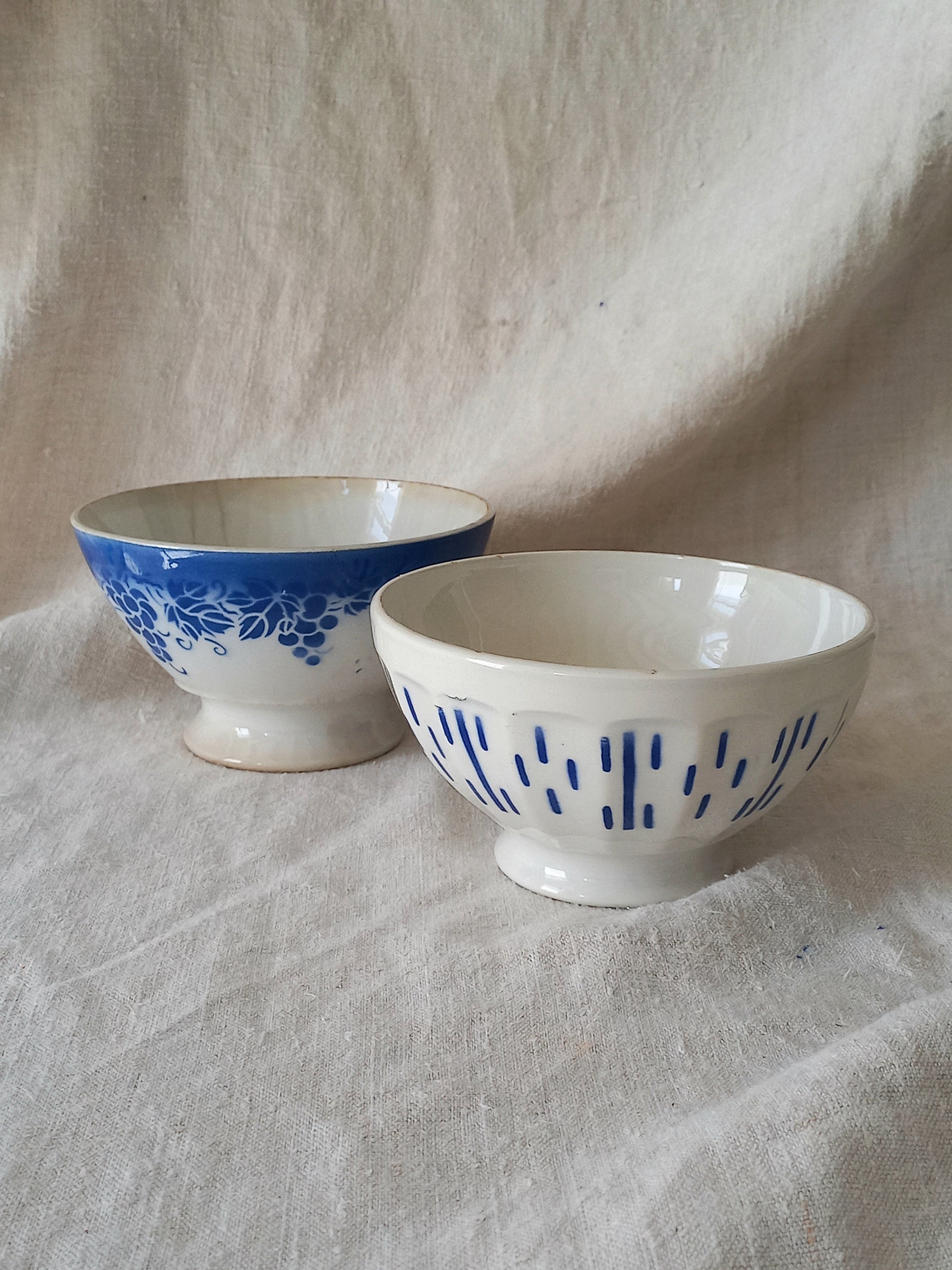 Blue and white vintage ceramic cafe au lait bowls with floral patterns on a light fabric background.