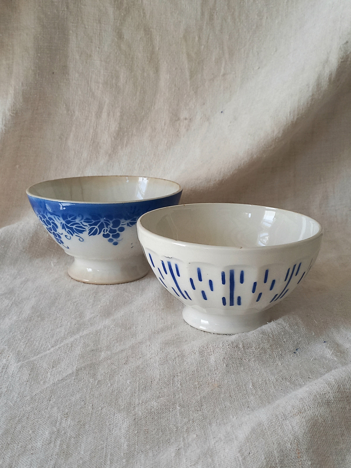 Blue and white vintage ceramic cafe au lait bowls with floral patterns on a light fabric background.