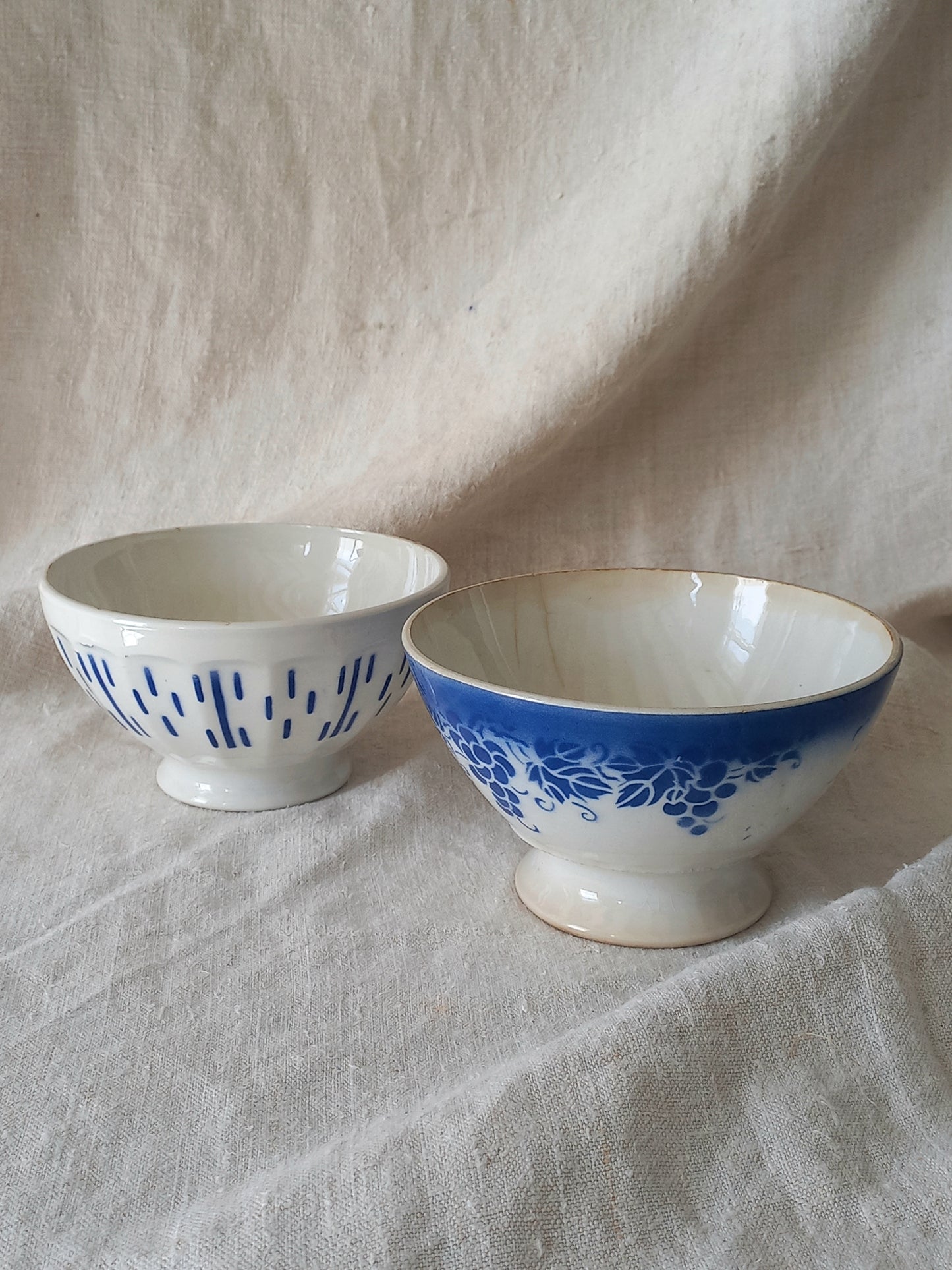 Blue and white vintage ceramic cafe au lait bowls with floral patterns on a light fabric background.