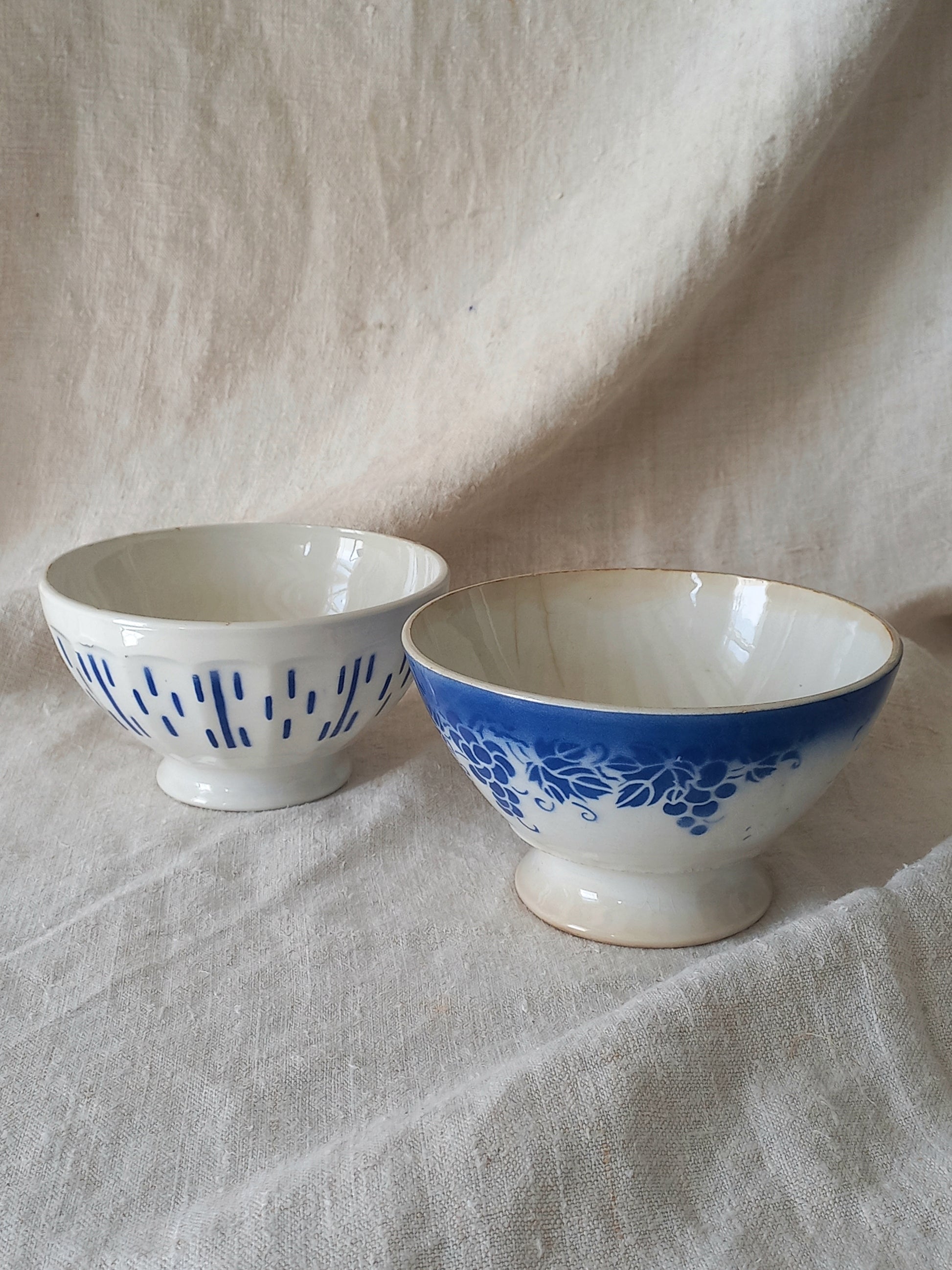 Blue and white vintage ceramic cafe au lait bowls with floral patterns on a light fabric background.