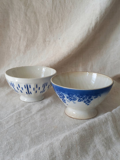 Blue and white vintage ceramic cafe au lait bowls with floral patterns on a light fabric background.
