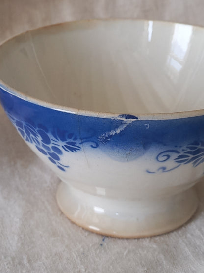 Blue and white vintage ceramic cafe au lait bowl with floral patterns on a light fabric background.