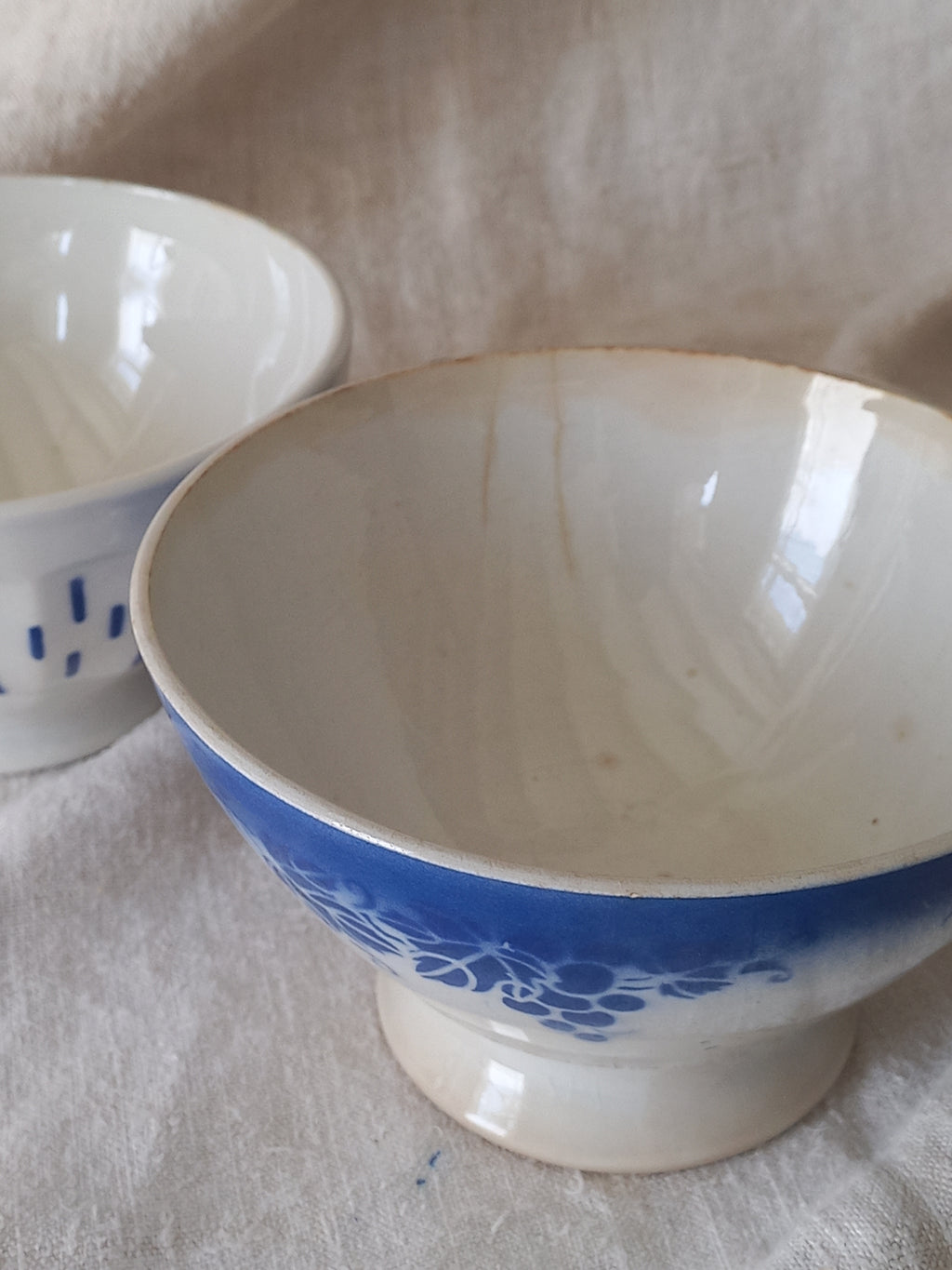 Blue and white vintage ceramic cafe au lait bowl with floral patterns on a light fabric background.