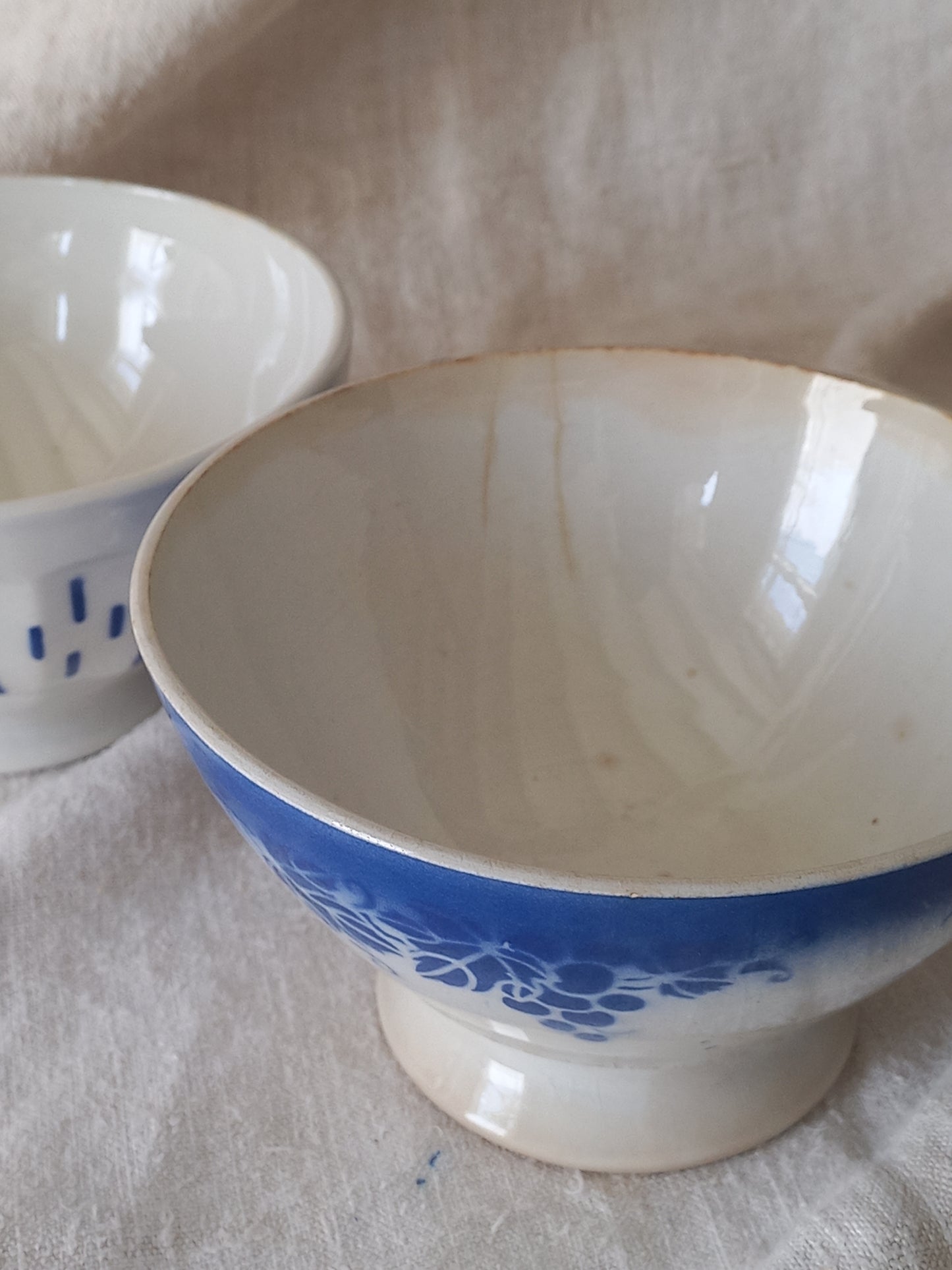 Blue and white vintage ceramic cafe au lait bowl with floral patterns on a light fabric background.
