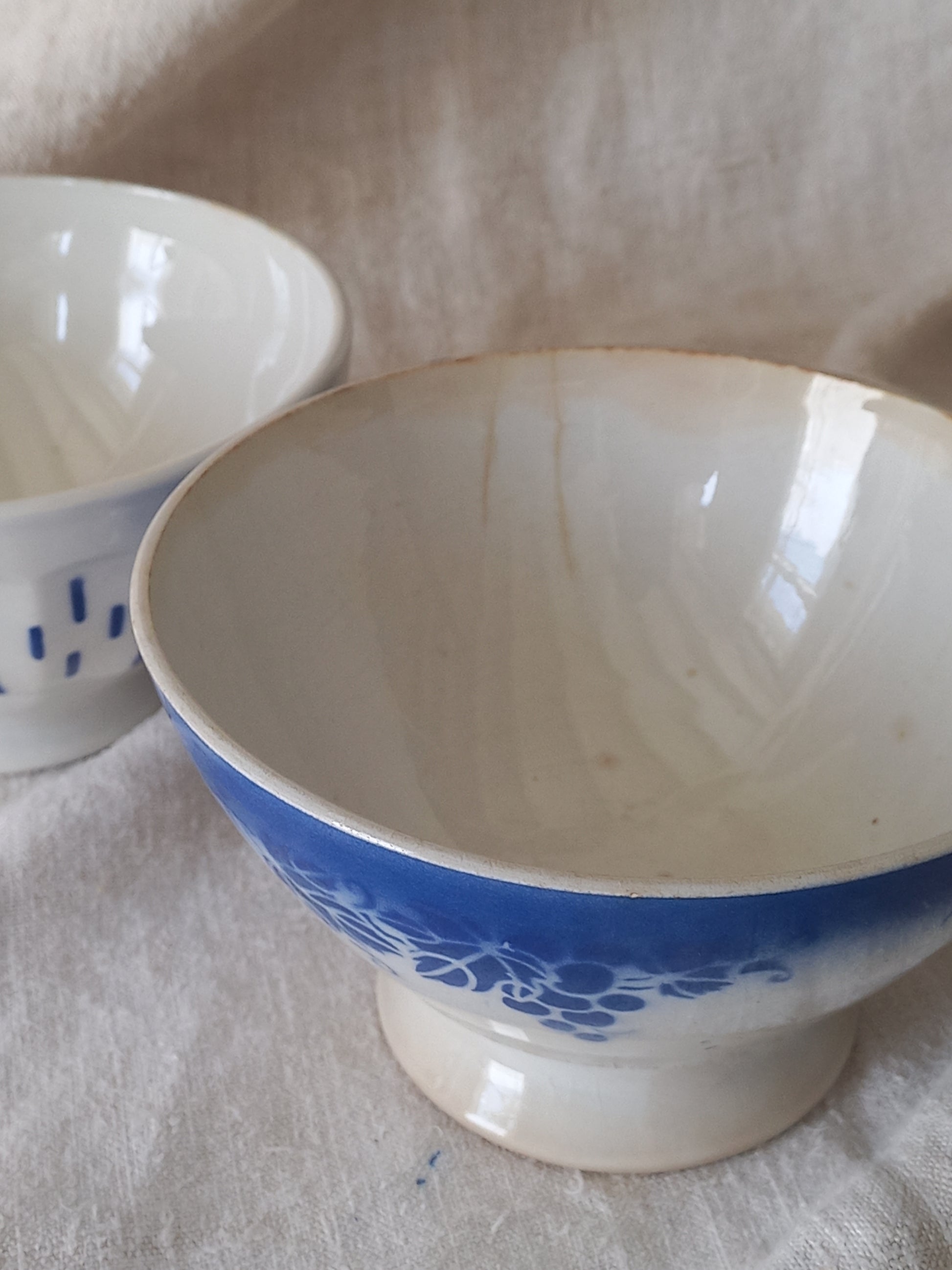 Blue and white vintage ceramic cafe au lait bowl with floral patterns on a light fabric background.