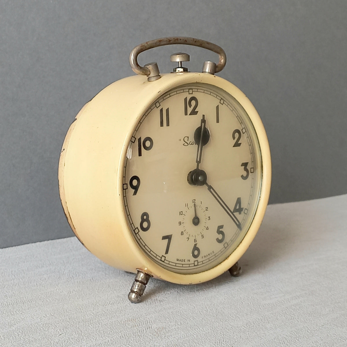 A wonderful French vintage alarm clock in a lovely shade of cream called 'Scout'.

This old clock is in working condition including the alarm and has a nice soothing ticking sound too.

The clock's metal case has a finish that has slight discoloring in places and paint chips (mainly to the rear - see photos) which gives it character.

In summary, a nice vintage alarm clock from France!