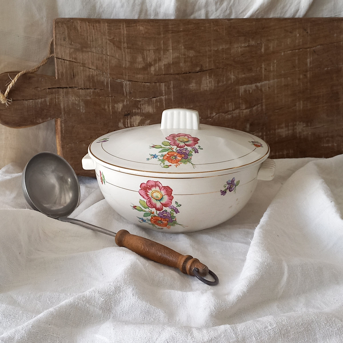 Decorative ceramic bowl with floral patterns on a wooden surface with a ladle.