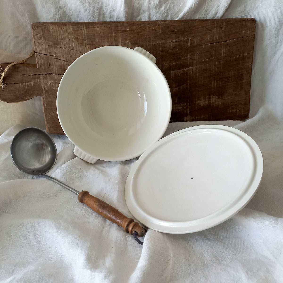 White ceramic bowl and lid with a wooden ladle on a white cloth background