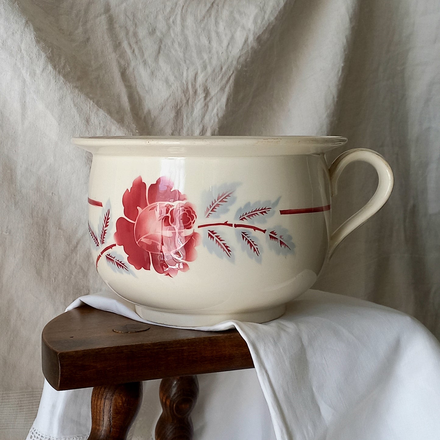 Vintage ceramic bowl with floral design on a wooden stool against a textured white background