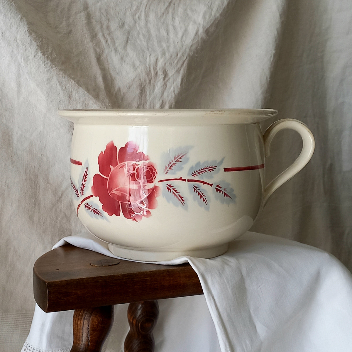 Vintage ceramic bowl with floral design on a wooden stool against a textured white background