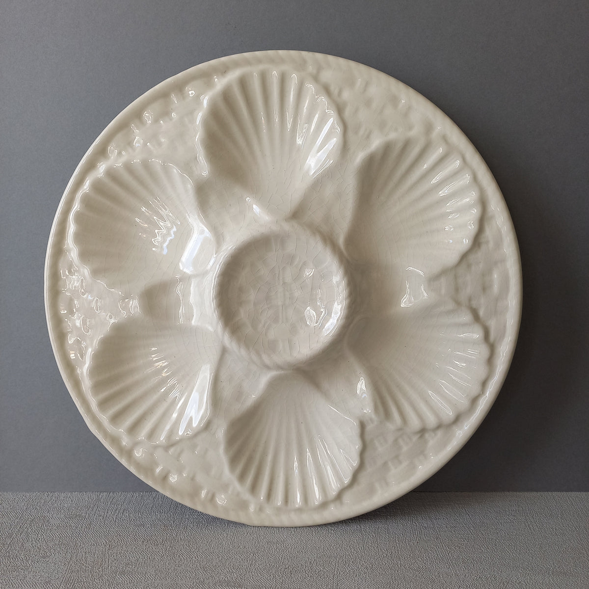 A beautiful French vintage oyster plate by Chantilly in a lovely shade of creamy white. This plate is a heavy, quality piece with six scalloped hollows for your oysters and a central hollow for a piece of lemon. There is a basket weave pattern and also a twisted rope pattern with some wonderful crazing in the glaze of this superb majolica plate which make it an eye catching piece of decor.