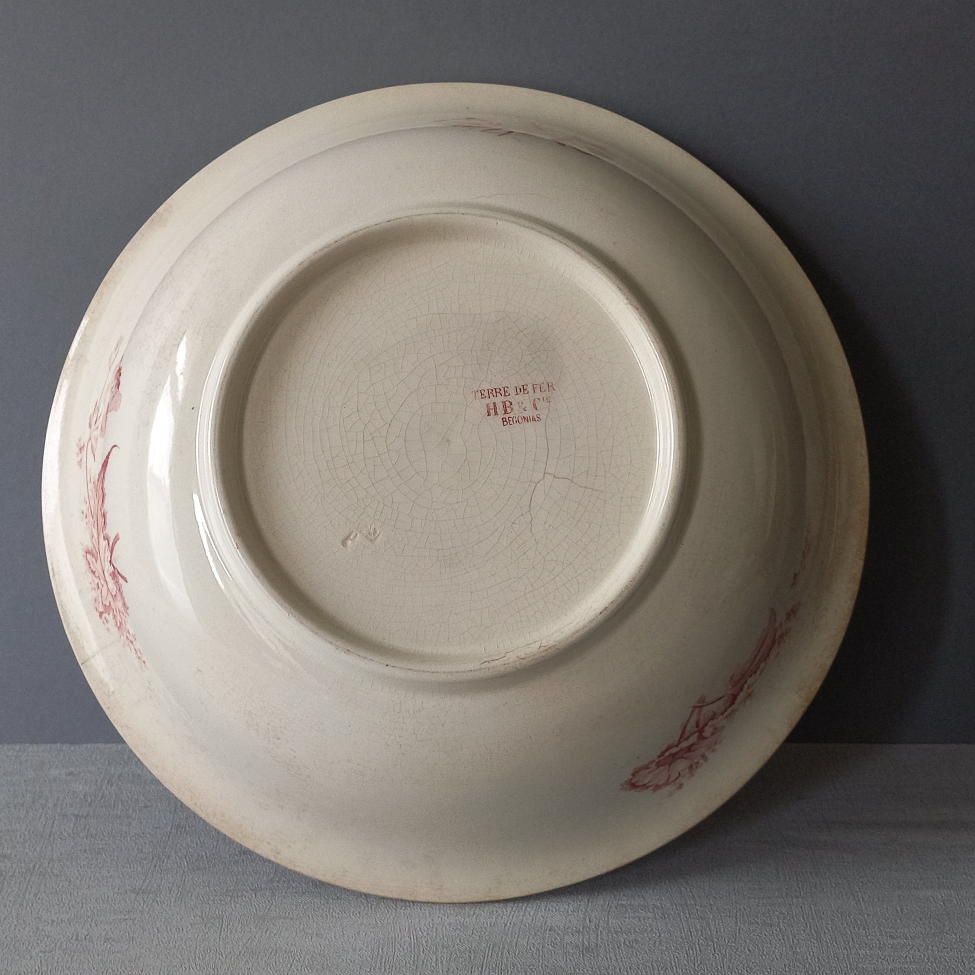 A large French vintage ironstone bowl with beautiful deep pink floral pattern on a creamy white base colour. Over the years this old bowl has aged nicely with crazing, tea-staining, and the odd little imperfections that show this as an authentic antique piece.

There is a maker's mark on the base. Circa. late 1800s/early 1900s.