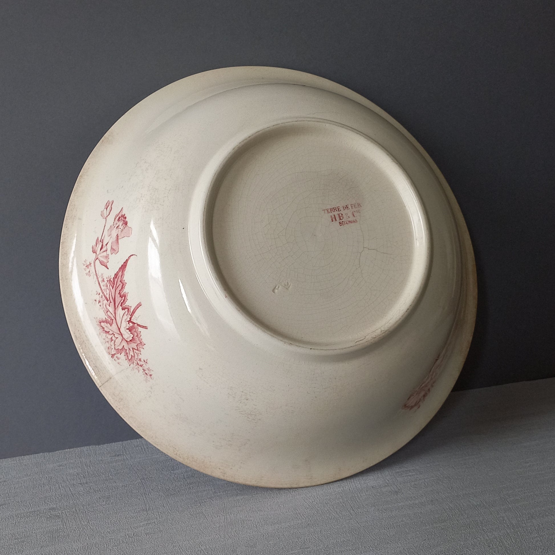 A large French vintage ironstone bowl with beautiful deep pink floral pattern on a creamy white base colour. Over the years this old bowl has aged nicely with crazing, tea-staining, and the odd little imperfections that show this as an authentic antique piece.

There is a maker's mark on the base. Circa. late 1800s/early 1900s.