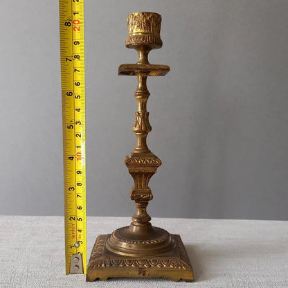 Decorative gold candlestick with a measuring tape for scale on a gray background
