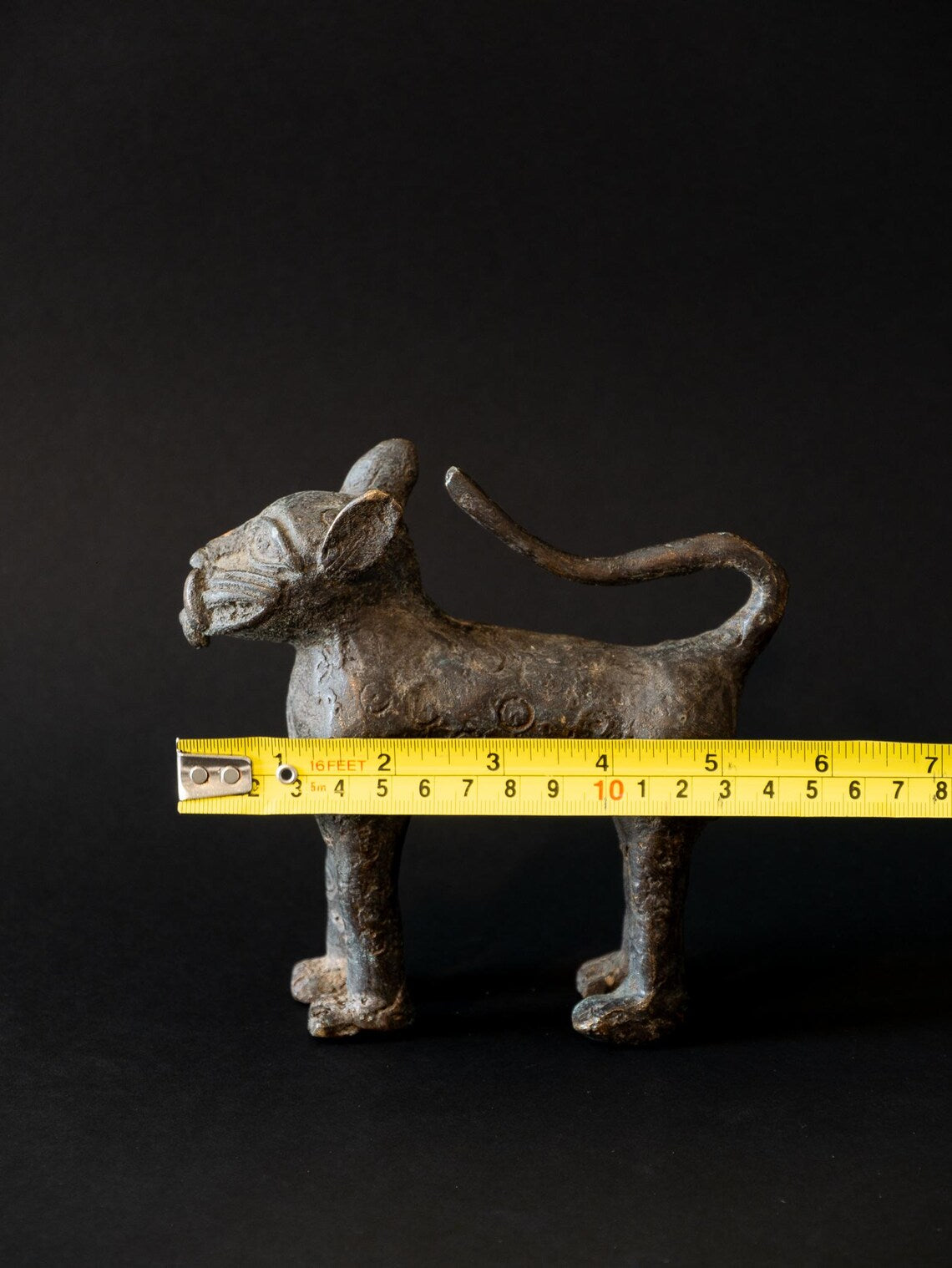 Metallic cat figurine with a measuring tape for scale on a black background