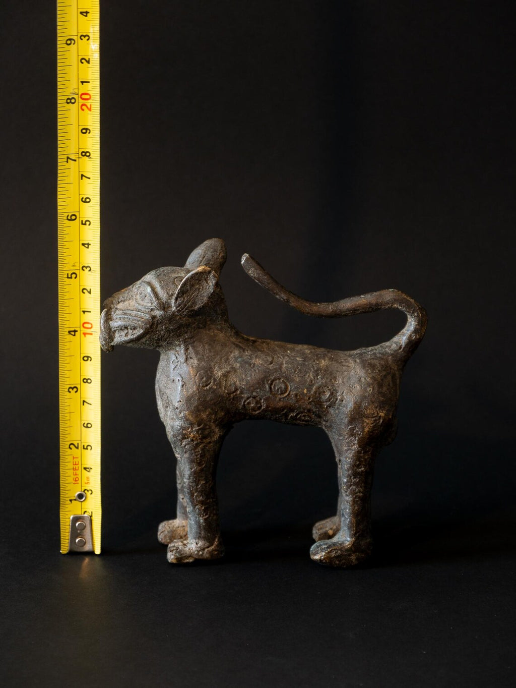 Bronze cat sculpture with a measuring tape for scale on a black background