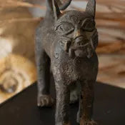 Bronze cat-shaped object on a dark surface with a blurred background