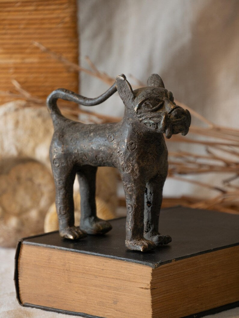 Decorative metal cat figurine on a book with a blurred natural background