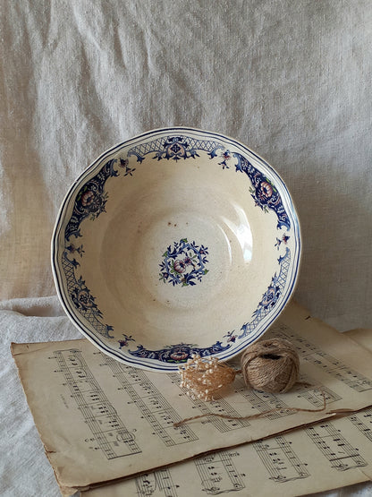 An antique blue and white patterned ceramic bowl displayed on top of antique sheet music, with twine in front, set against a draped beige linen backdrop.