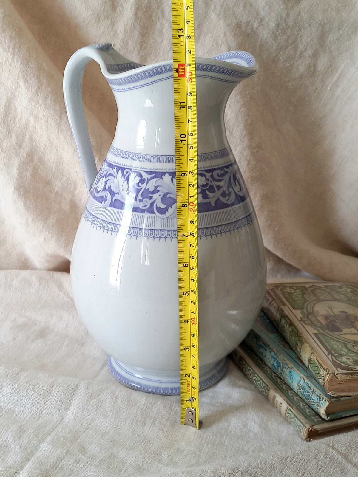 Antique ironstone pitcher in white with a rare lavender colour decorative pattern in a decorative setting with a tape measure for reference.
