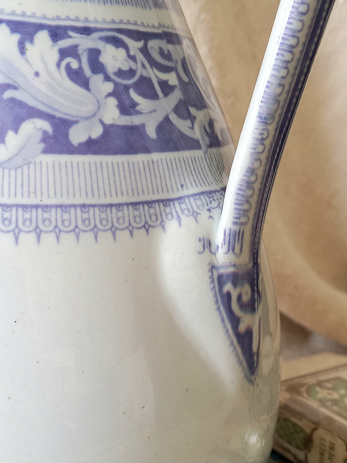 Close-up of an antique ironstone pitcher in white with a rare lavender colour decorative pattern in a decorative setting.