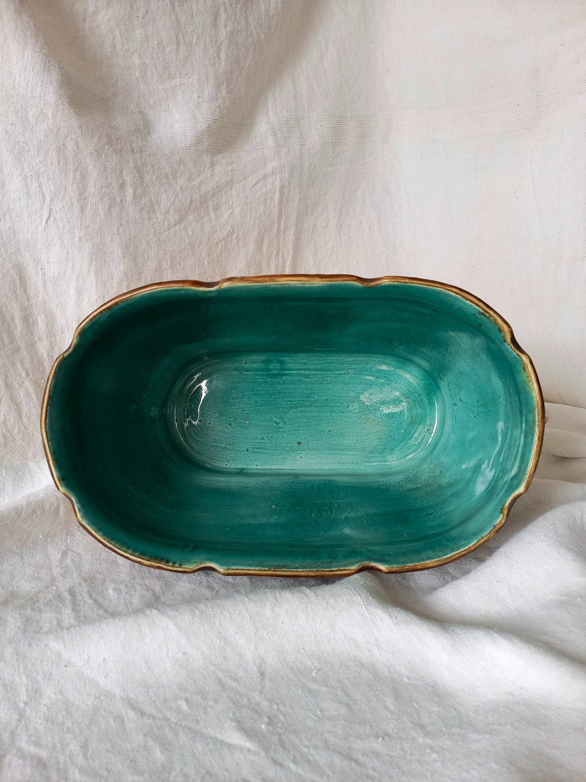 An oval antique majolica planter interior photographed on a draped cream fabric background.