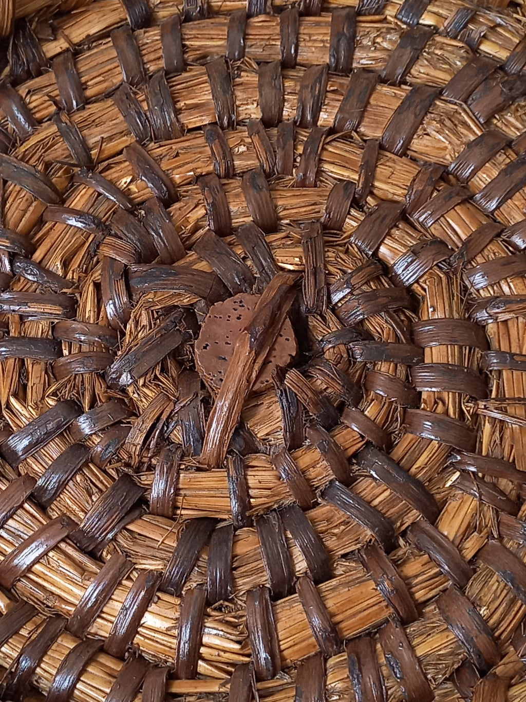 Close-up of a woven natural fiber vintage basket with a spiral pattern of light tan and dark brown strips, featuring a small cork in the center.