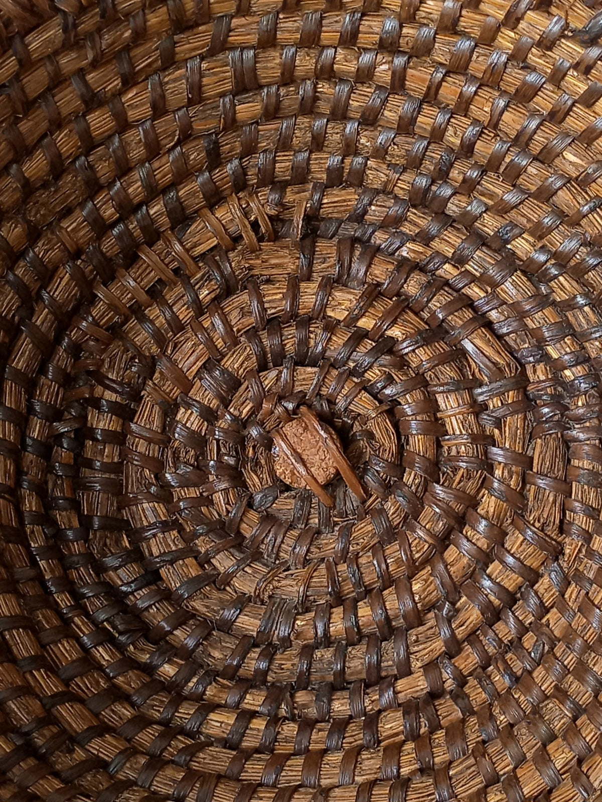 Close-up of a woven vintage basket with a spiral pattern made from natural brown and dark brown fibers.