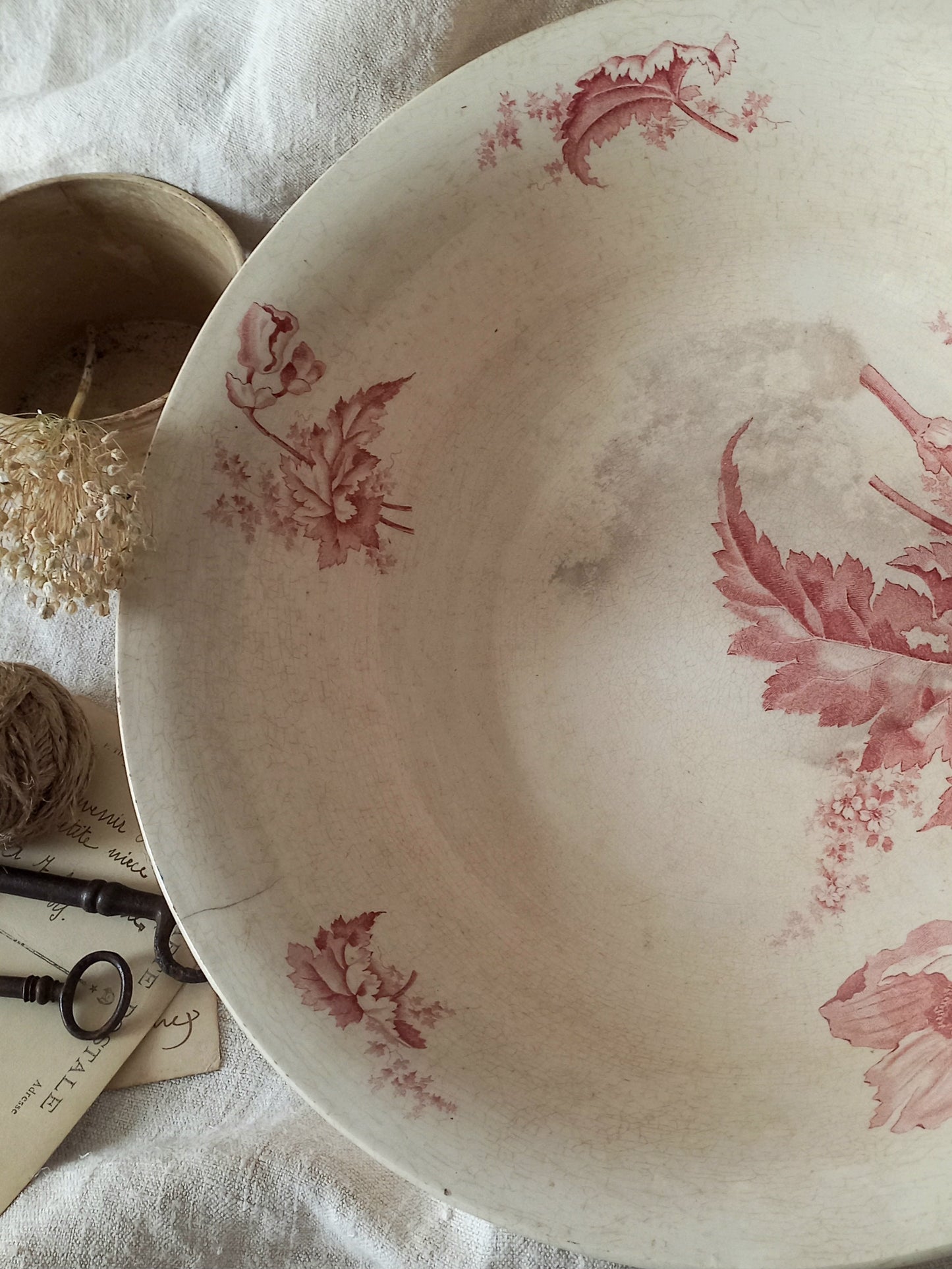 A large French ironstone bowl with deep pink floral pattern on a creamy white base. This antique piece has aged naturally over time, showing fine crazing, tea-staining, and small imperfections that reflect its long history.
