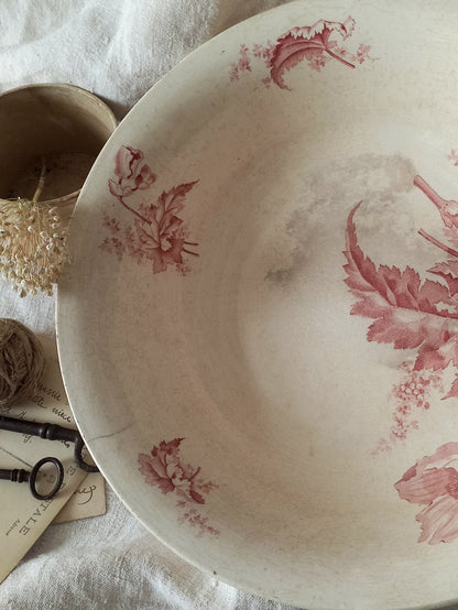 A large French ironstone bowl with deep pink floral pattern on a creamy white base. This antique piece has aged naturally over time, showing fine crazing, tea-staining, and small imperfections that reflect its long history.