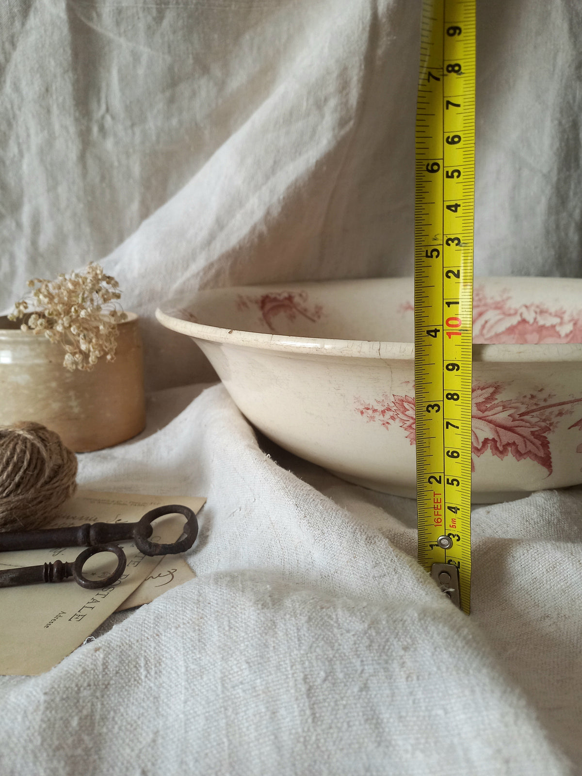 A large French ironstone bowl with deep pink floral pattern on a creamy white base. This antique piece has aged naturally over time, showing fine crazing, tea-staining, and small imperfections that reflect its long history.
