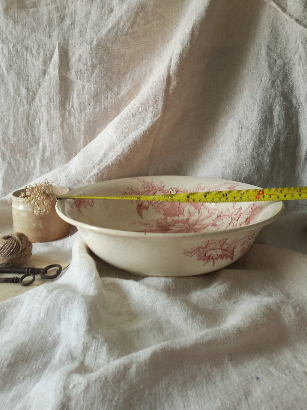 A large French ironstone bowl with deep pink floral pattern on a creamy white base. This antique piece has aged naturally over time, showing fine crazing, tea-staining, and small imperfections that reflect its long history.