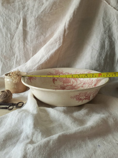 A large French ironstone bowl with deep pink floral pattern on a creamy white base. This antique piece has aged naturally over time, showing fine crazing, tea-staining, and small imperfections that reflect its long history.