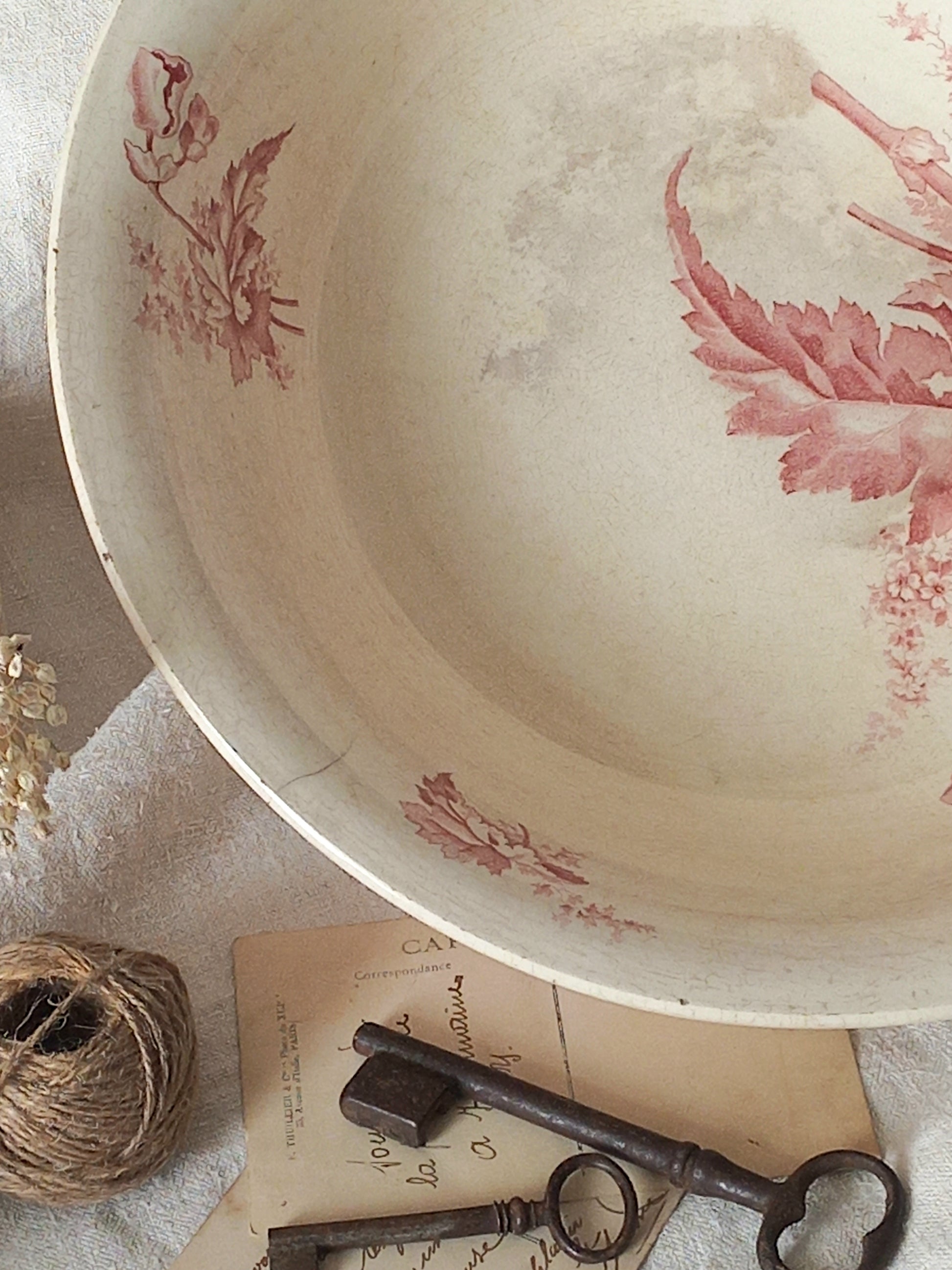 A large French ironstone bowl with deep pink floral pattern on a creamy white base. This antique piece has aged naturally over time, showing fine crazing, tea-staining, and small imperfections that reflect its long history.
