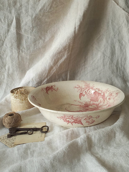 A large French ironstone bowl with deep pink floral pattern on a creamy white base. This antique piece has aged naturally over time, showing fine crazing, tea-staining, and small imperfections that reflect its long history.