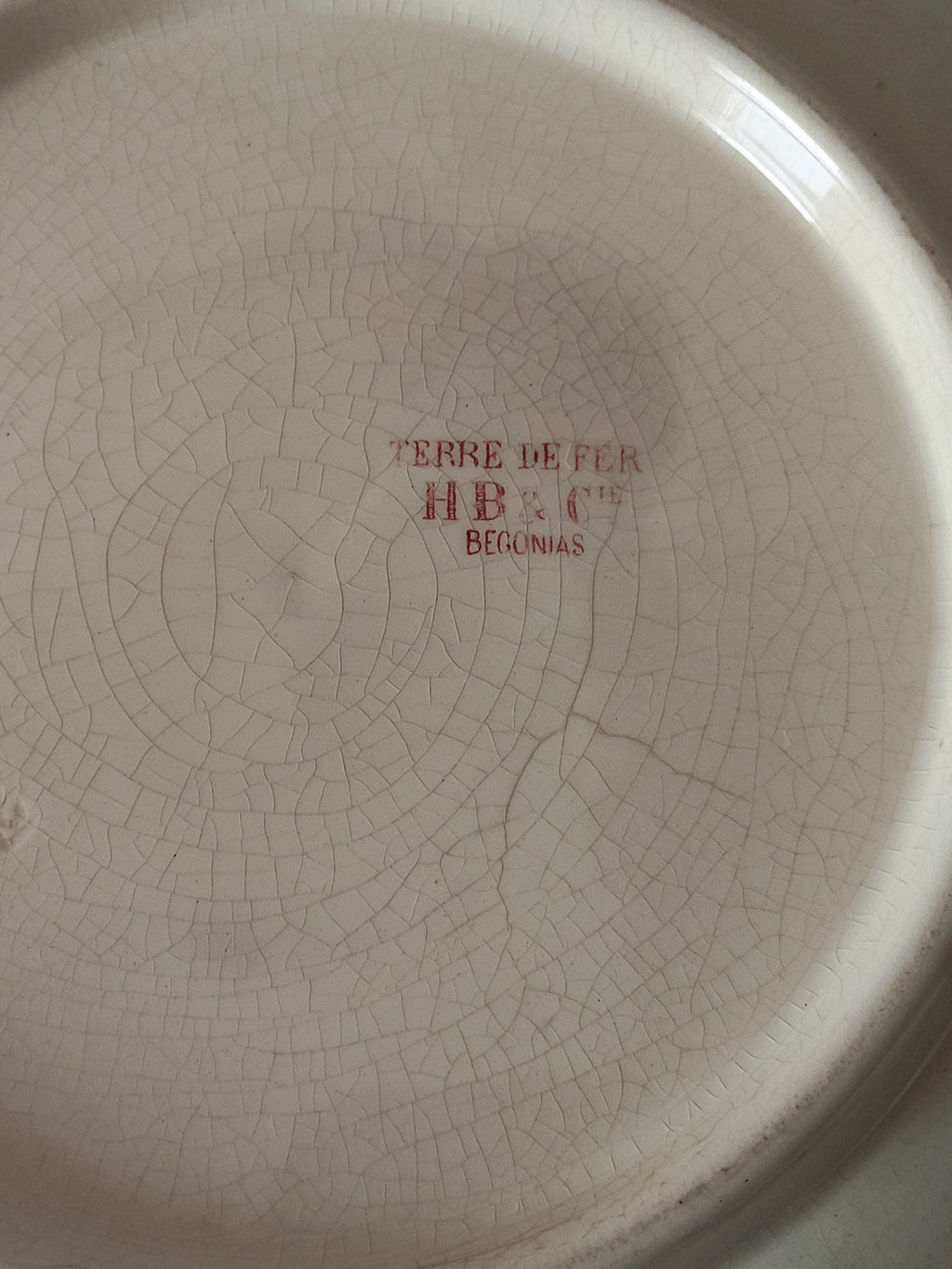A large French ironstone bowl with deep pink floral pattern on a creamy white base. This antique piece has aged naturally over time, showing fine crazing, tea-staining, and small imperfections that reflect its long history.