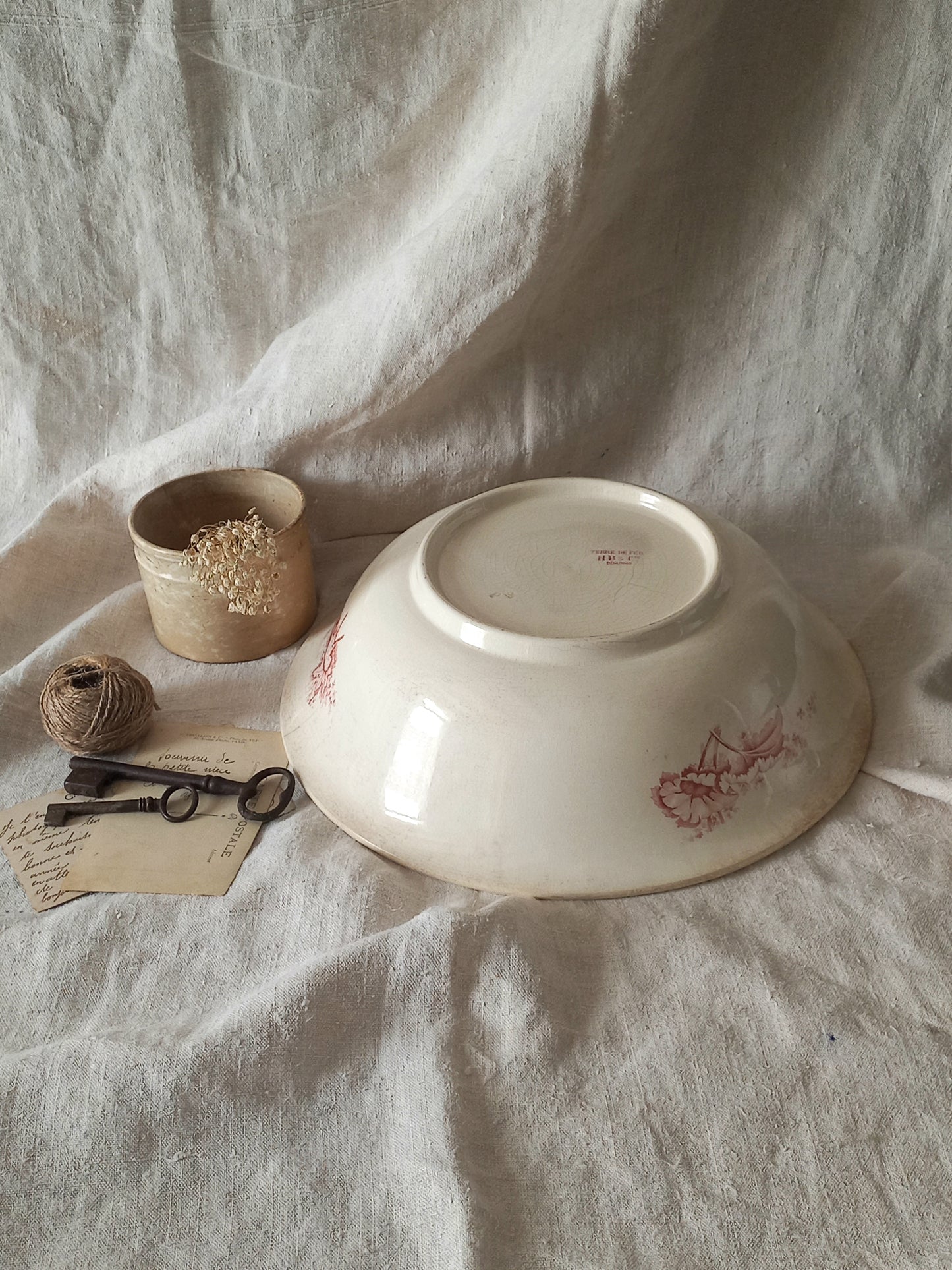 A large French ironstone bowl with deep pink floral pattern on a creamy white base. This antique piece has aged naturally over time, showing fine crazing, tea-staining, and small imperfections that reflect its long history.