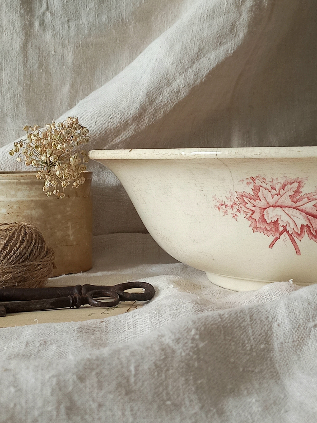 A large French ironstone bowl with deep pink floral pattern on a creamy white base. This antique piece has aged naturally over time, showing fine crazing, tea-staining, and small imperfections that reflect its long history.