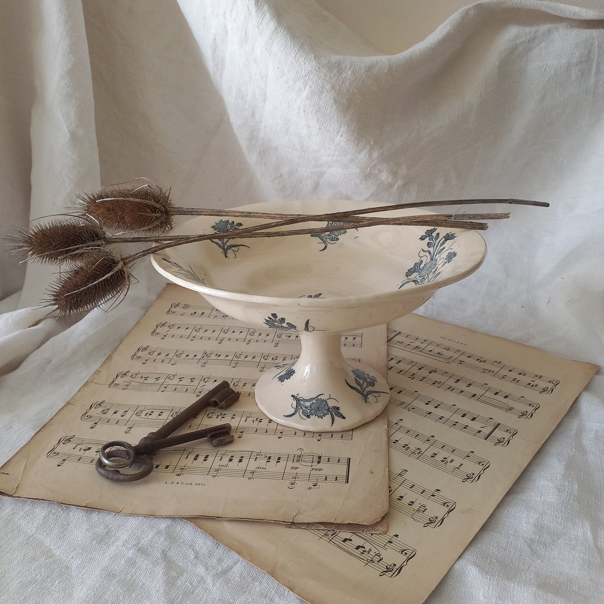 A beautiful antique compote or footed bowl by French manufacturer Longchamp. The main colour is a warm cream/white with blue floral transferware pattern.