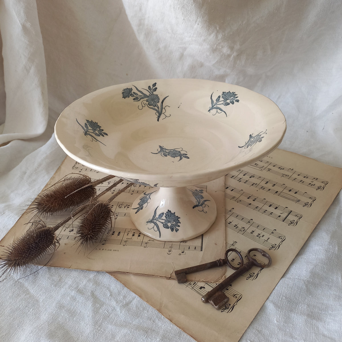 A beautiful antique compote or footed bowl by French manufacturer Longchamp. The main colour is a warm cream/white with blue floral transferware pattern.
