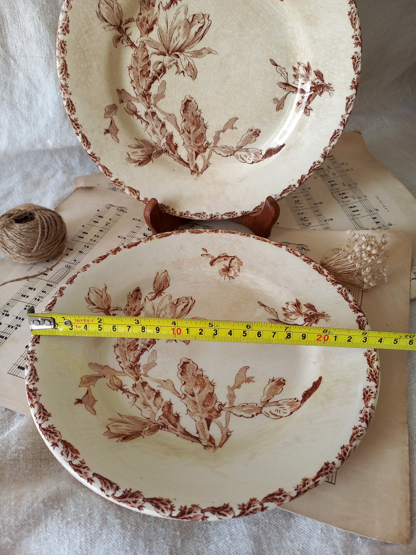 Two ceramic plates with floral patterns on a surface with a measuring tape for scale