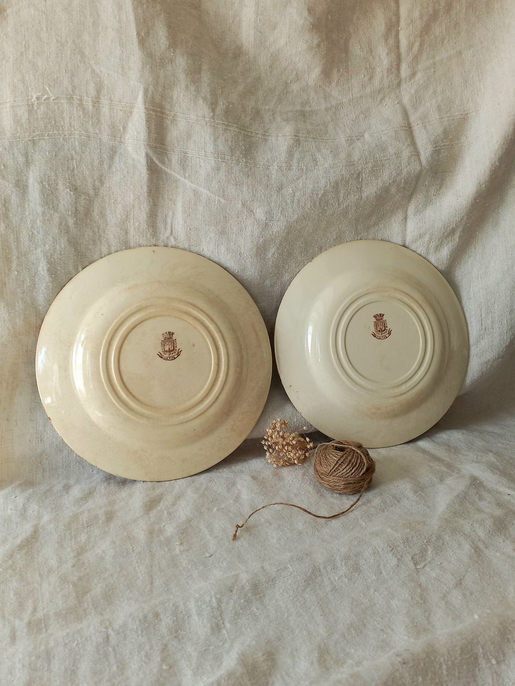 Two ceramic plates with a logo on a textured fabric background.