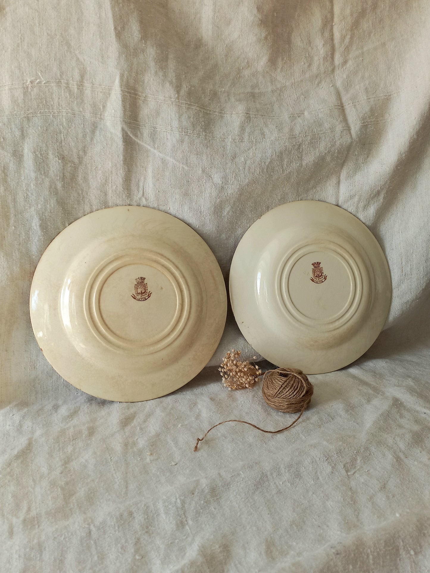Two ceramic plates with a logo on a textured fabric background.