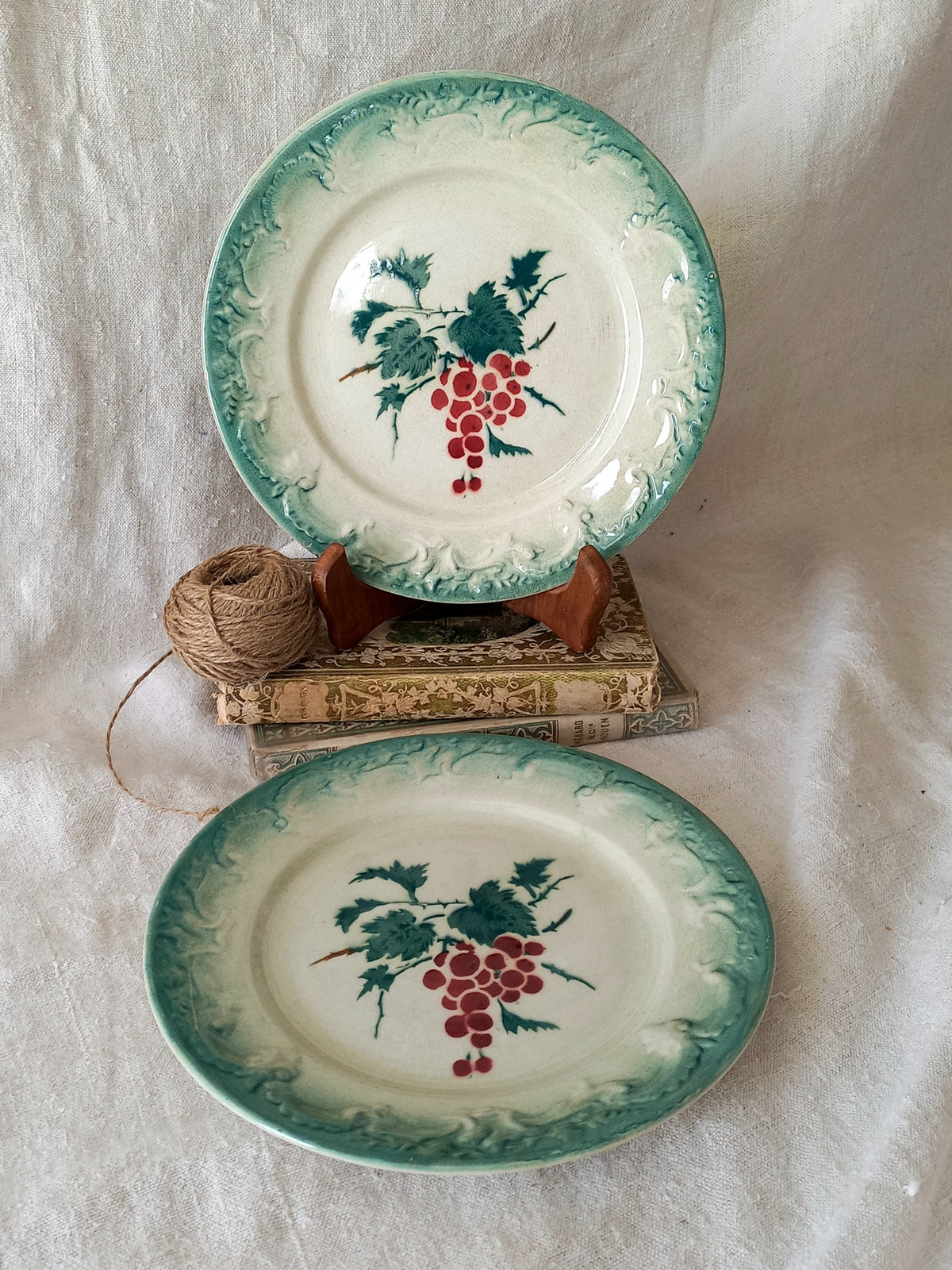 Two ceramic plates with grape design on a textured white surface