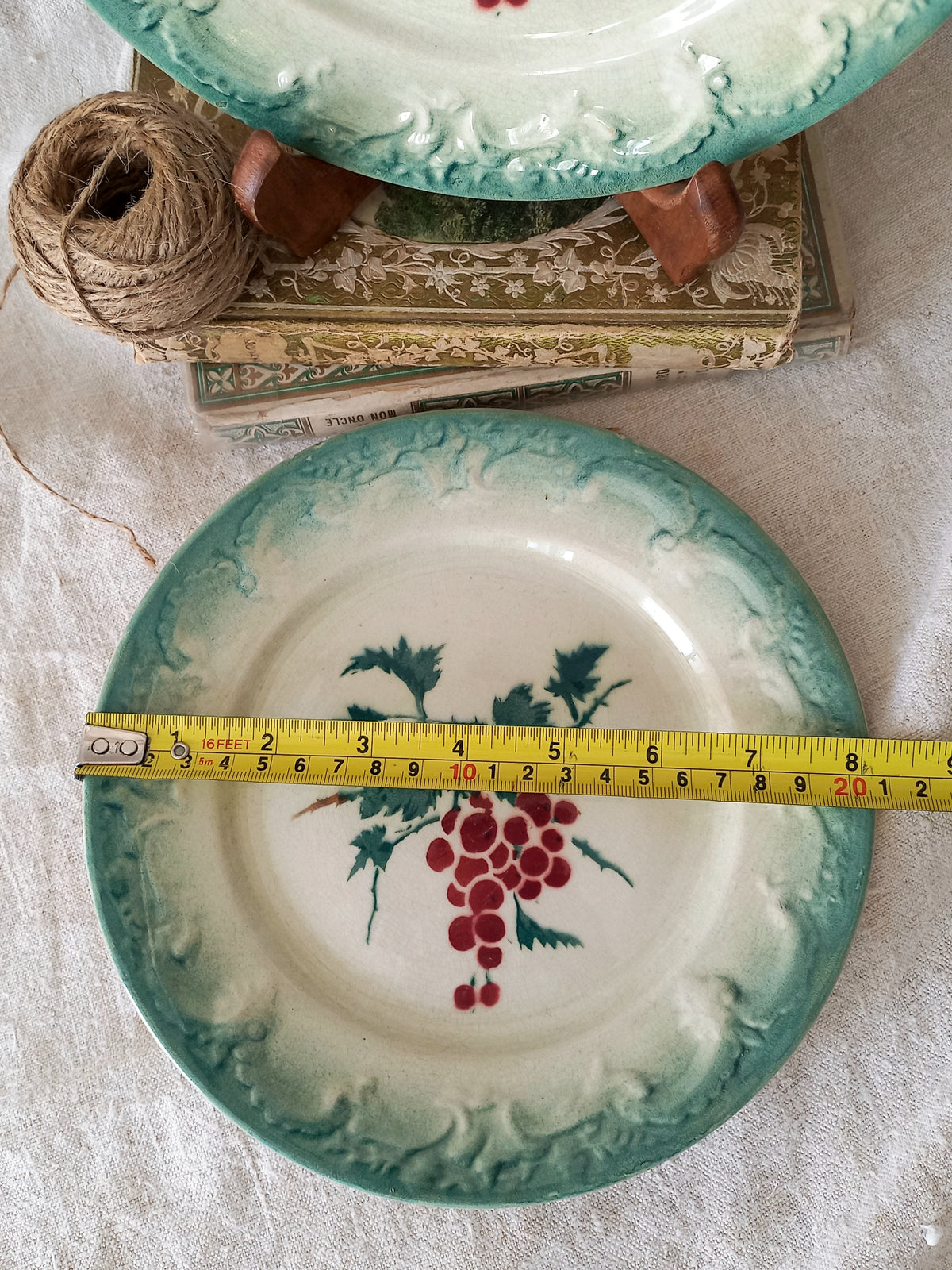 Decorative plate with grape design and measuring tape for scale, placed on a textured surface.
