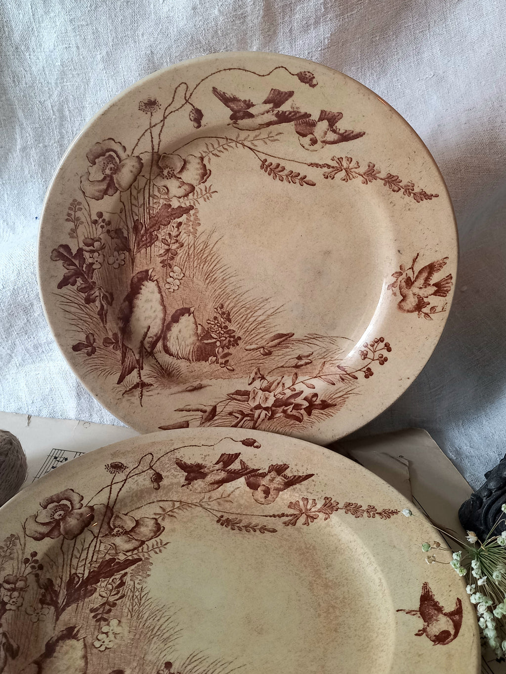Two ceramic plates with brown floral and animal design on a white fabric background