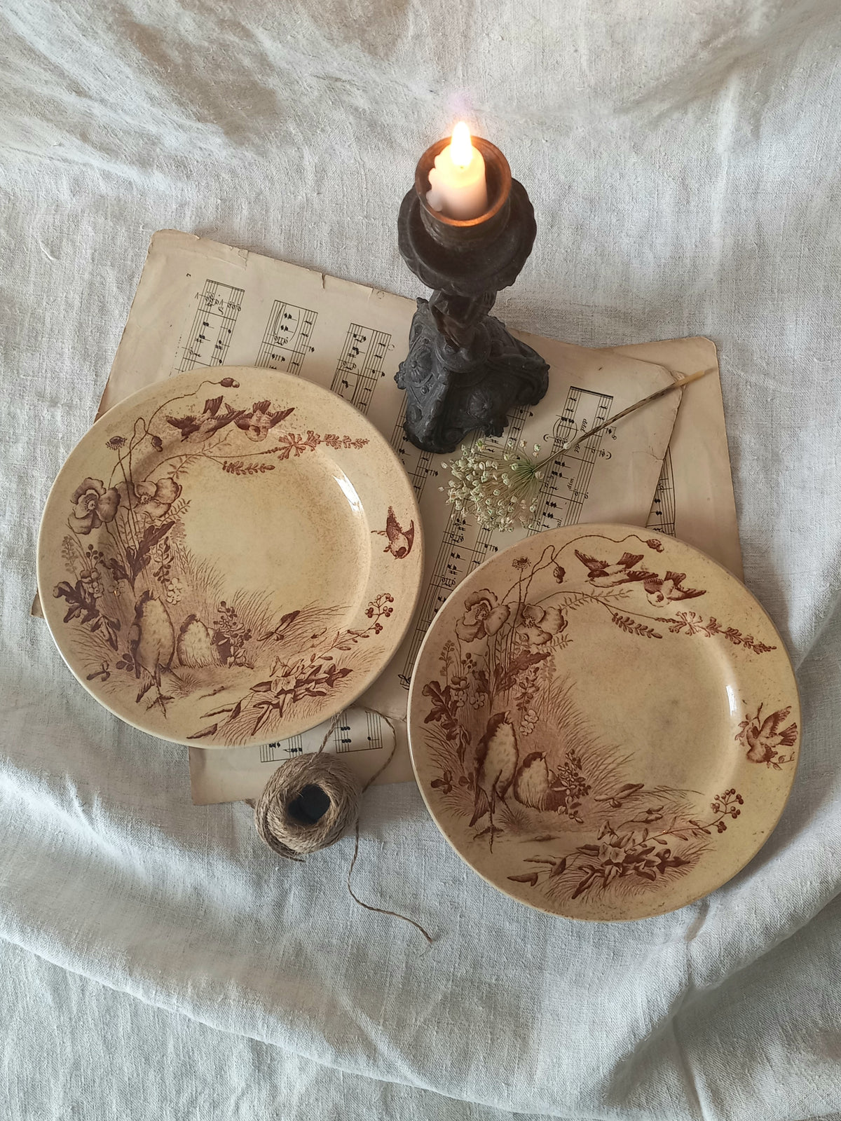 Two decorative plates with intricate designs on a white fabric background with a candle.