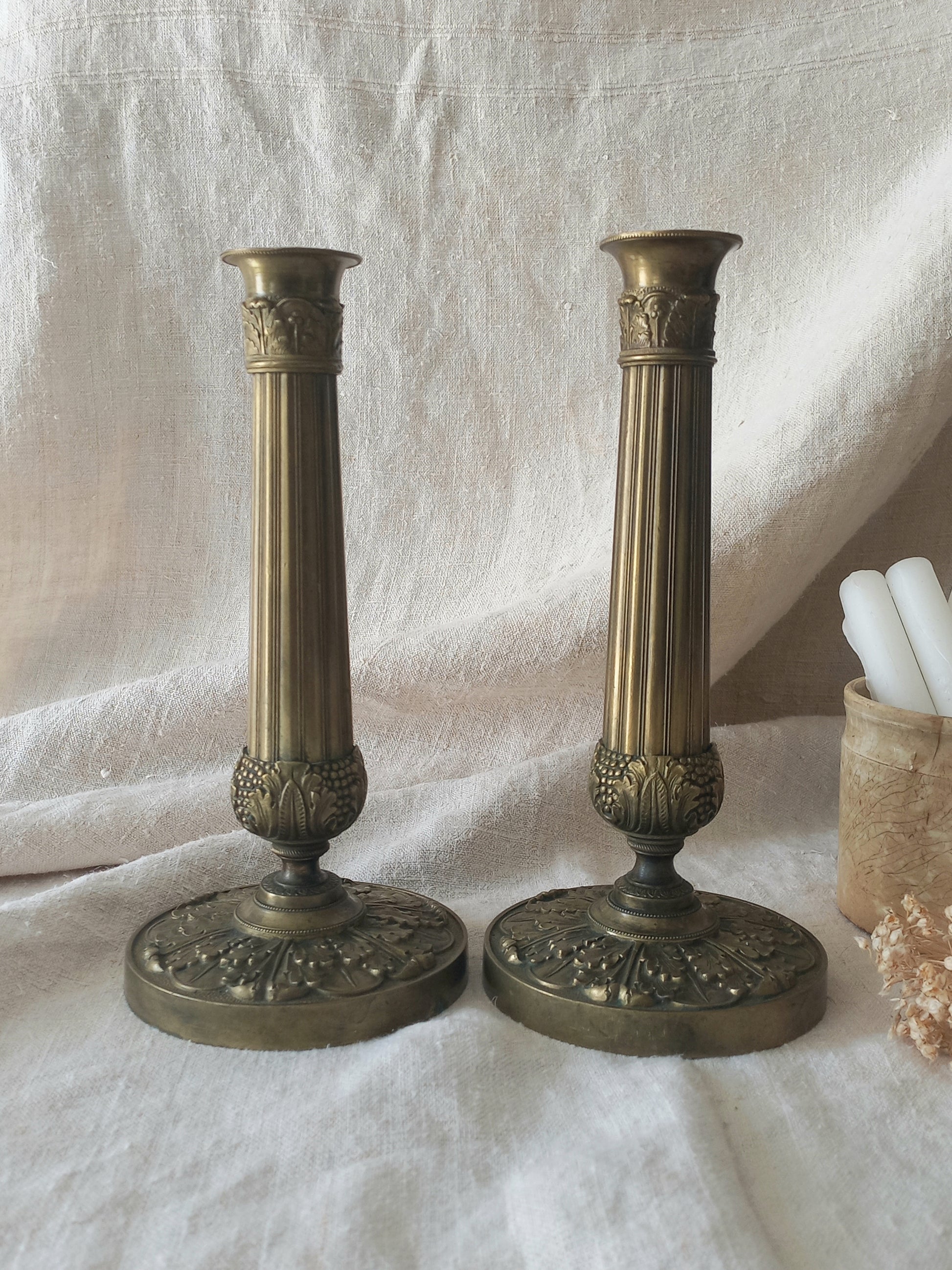 Pair of beautiful French antique decorative candle holders with Empire styling on a beige background.