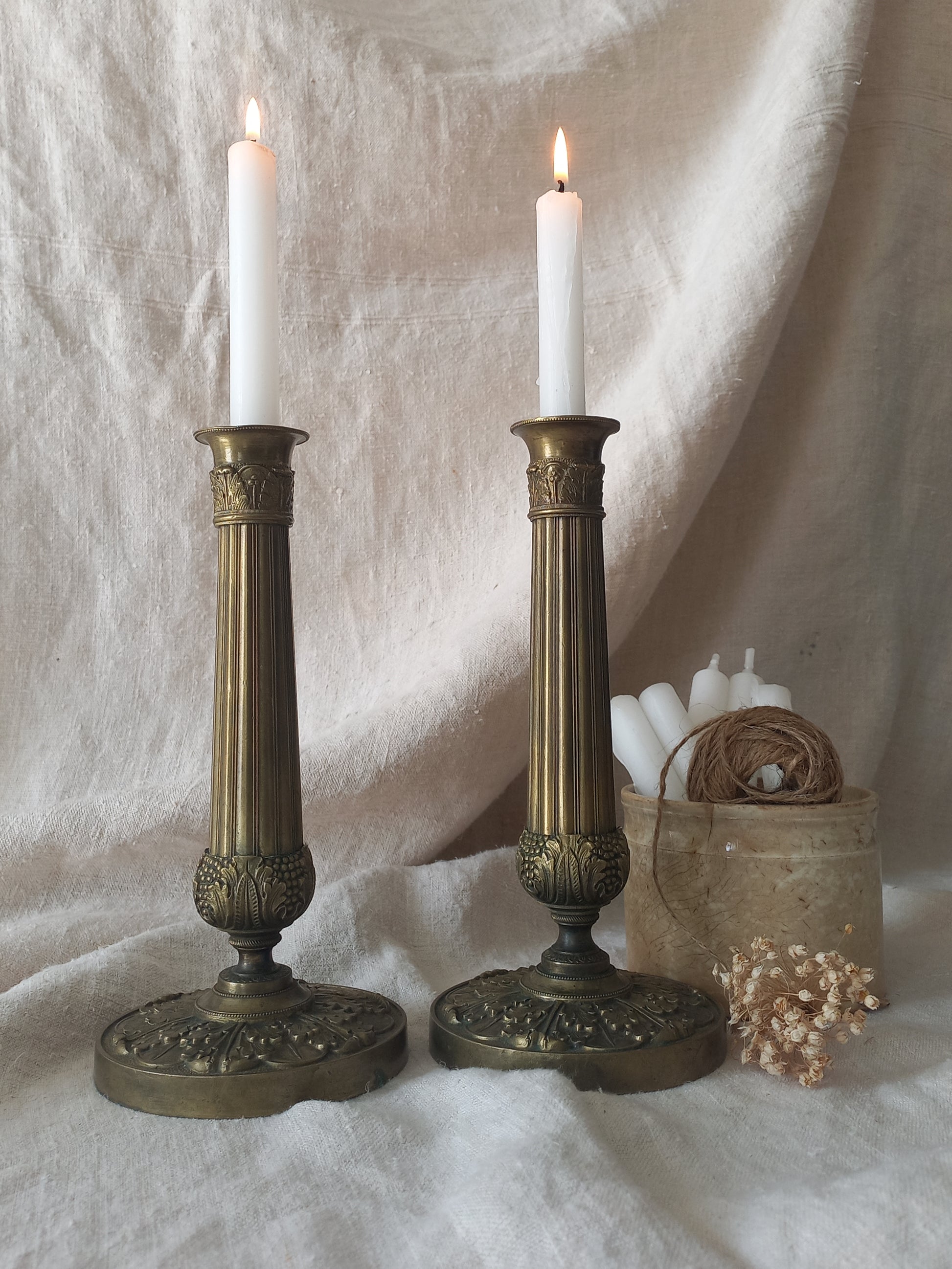Two brass candlesticks with lit candles on a textured white surface.