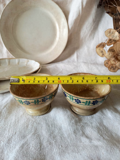 Two ceramic bowls with floral patterns on a white cloth, measured with a tape measure.